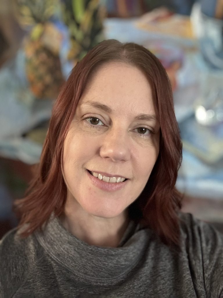 A picture of Heidi Rabe, a white SLP with shoulder length red-brown hair and brown eyes, smiling into the camera. 